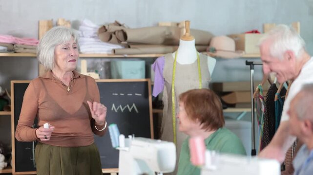 Seamstress explaining sewing techniques to older adults in training workshop