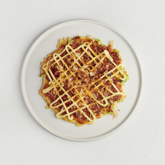 Top view of okonomiyaki with mayo and bonito flakes on white plate, selective focus