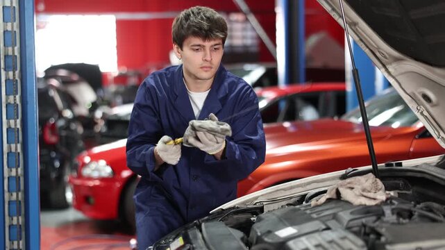 Qualified mechanic in a car service checks the amount of oil in the car with a dipstick. Car service employee inspects the car and changes the engine oil. High quality 4k footage