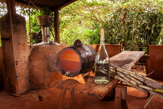 Artisanal cachaca production in Brazil. A rustic scene with a copper still, sugarcane stalks, a wooden barrel, and a bottle of the traditional Brazilian spirit, the craft distillation process.