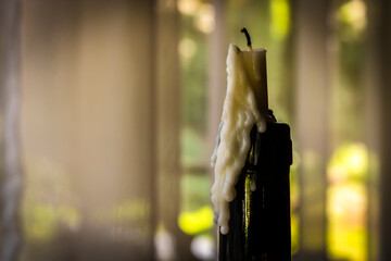 An extinguished white candle with melted wax dripping down a dark glass bottle. The scene is set...