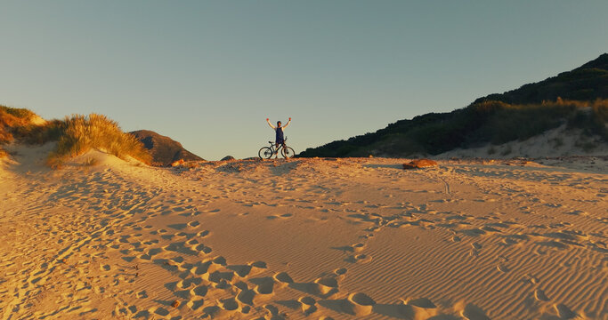 Dune, bicycle and man with celebration for sunset view, travel and fitness for journey with banner. Person, cycling and explore for exercise, eco tourism and nature space for holiday or vacation