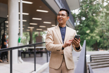 Asian businessman smiling using smartphone outdoors
