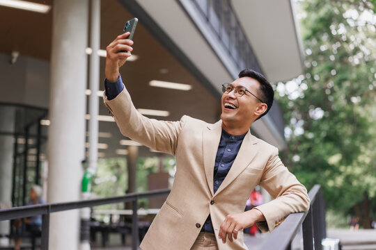 Happy asian man taking selfie with smartphone outdoors