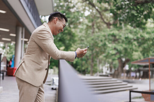 Asian businessman smiling and checking smartphone outdoors