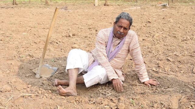 Unhappy sad rural indian farmer sitting on arid farmland touching soil. Concept of drought crisis in agricultural land in india. No rain no water. Climate change.