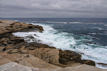 The rugged beauty of the Atlantic Ocean as seen from Peggy's Cove in Nova Scotia, with waves crashing against the rocky shore under an overcast sky.