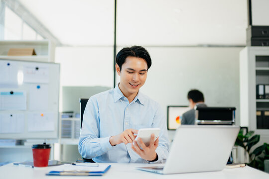 Confident  Asian businessman typing laptop computer and digital tablet while holding coffee at office