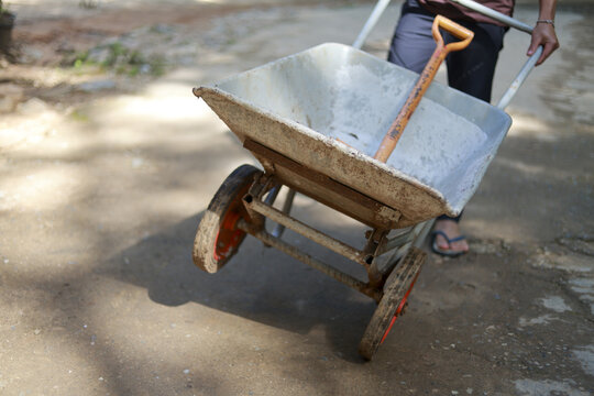 Determined worker pushing wheelbarrow with shovel at construction site. Manual labor involves moving heavy material for building, representing hard work and industry