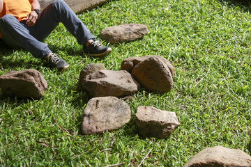 Person sitting on green grass lawn outdoor in garden. collection of natural rock and stone scattered on ground. calm and relaxing scene of landscaping project