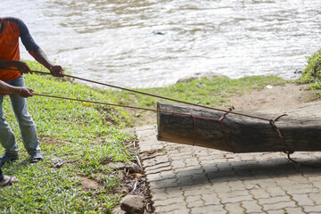 Two man showing teamwork and effort, pulling heavy log with rope from river bank. display of hard...