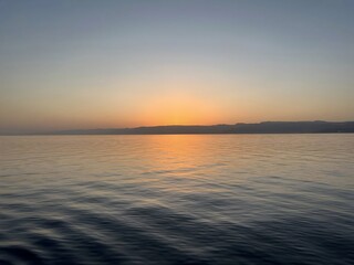 The image depicts a tranquil body of water extending to the horizon, with gentle ripples on the surface. In the background, a distant landmass or shoreline stretches across the scene