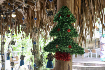 Festive green tinsel christmas tree decoration hanging outdoors from wooden post. This cheerful holiday ornament brings holiday spirit to tropical rustic setting