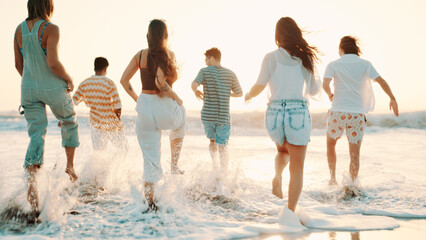 People, friends and running with water splash on beach for summer vacation, sunset or playful day. Group, community or playing with waves on ocean coast or sea for weekend getaway or fun holiday