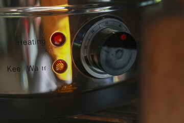Close up of stainless steel kitchen appliance knob. Control dial set to specific temperature for cooking. Two warm indicator lights glowing on shiny metallic surface
