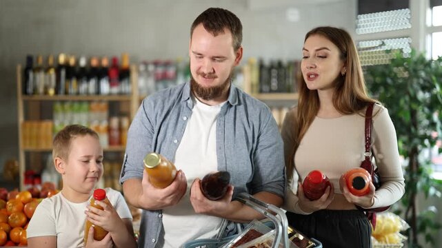Family with son choose tasty juice together in grocery section of a supermarket. High quality 4k footage