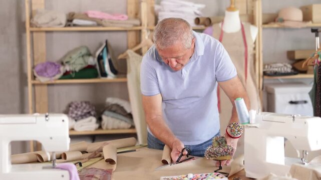 Mature man cutting paper in sewing workshop. Tailor makes patterns for clothes. High quality 4k footage