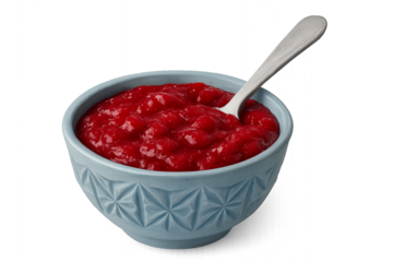 A vibrant red chunky cranberry sauce with whole berries is served in a light blue ceramic bowl with a geometric pattern and a silver spoon for a traditional holiday meal