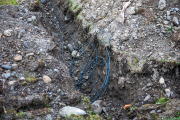 Exposed cables in a dug trench in rocky soil, showing ground work during outdoor installation.