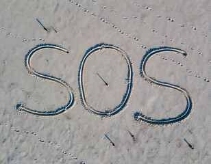 giant ‘SOS’ traced in sand on beach, top-down drone view, lone footprints nearby