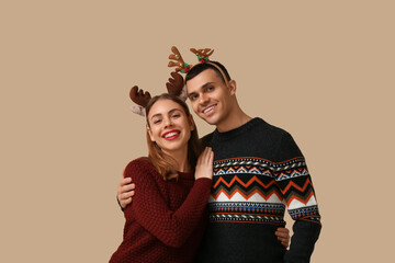 Happy young couple in reindeer horns on beige background