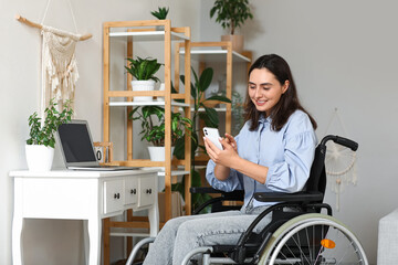 Young woman in wheelchair using mobile phone at home