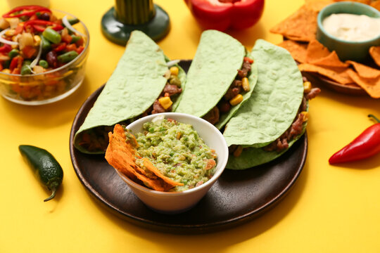 Plate with traditional Mexican tacos and guacamole on yellow background. Cinco de Mayo (Fifth of May) celebration
