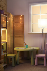 Interior of stylish children's room with cozy armchair, toys, glowing lights and folding screen at night