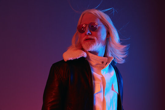 Stylish man with long white hair and sunglasses posing against a colorful background, showcasing modern fashion and a charismatic vibe in a striking portrait