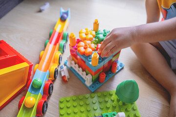 Close-up of a child’s hand playing with colorful plastic building blocks. Articles about children’s play or imagination and motor skill development.