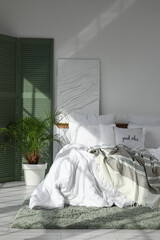Interior of light bedroom with green folding screen, palm tree and painting