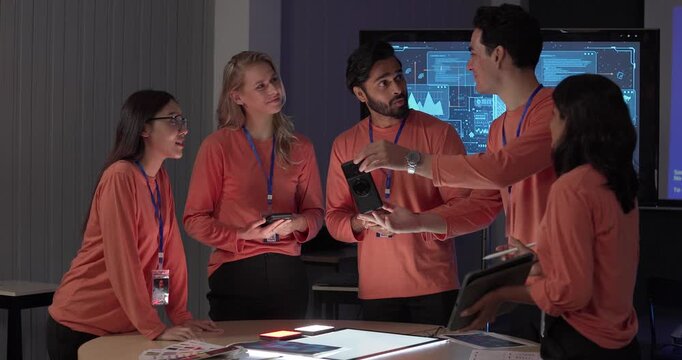 Product team in matching orange shirts collaborates around table, reviewing wireframes, color swatches, mobile app prototypes with analytics dashboards. Capturing UX UI sprint planning session
