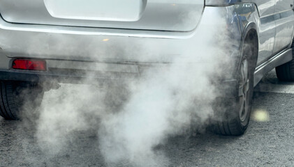 Car exhaust smoke polluting air upon urban street, closeup view of rear bumper and tires within...