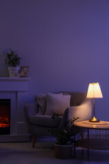 Fototapeta premium Interior of dark living room with glowing lamp, armchair and fireplace at night