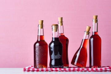Four Elegant Glass Bottles of Red Drink on a Pink Background with a Red Linen Napkin
