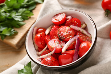 Bowl of fresh tomato salad with red onion and parsley on wooden background, closeup