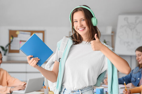 Female student with headphones and notebook showing thumb-up in classroom
