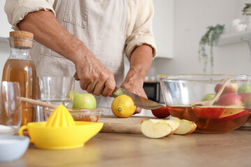 Mature man cutting lemon for apple cider in kitchen, closeup