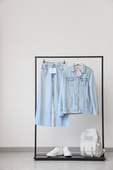 Rack with denim clothes, sneakers and backpack near light wall
