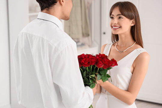 Beautiful young woman receiving red roses from her boyfriend at home