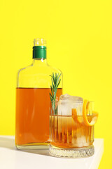 Glass of tasty Old Fashioned cocktail with rosemary on white table against yellow background
