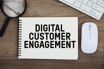 Digital Customer Engagement text written on notepad with keyboard, optical mouse and magnifying glass on wooden background