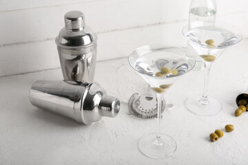 Glasses of tasty martini cocktail with green olives and shakers on light table