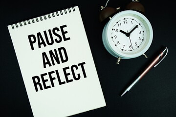 Pause And Reflect text written on notepad with pen and alarm clock