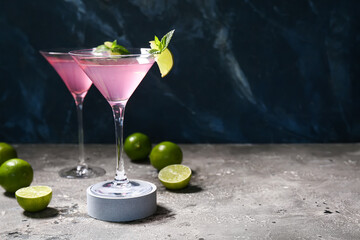 Glasses of tasty Cosmopolitan cocktail garnished with lime and mint on grey table against blue background