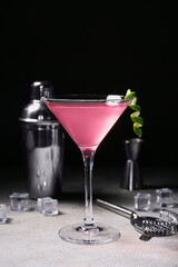Glass of tasty Cosmopolitan cocktail and ice cubes on white table against black background
