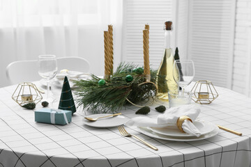 Beautiful Christmas table setting with gift box, candles and bottle of champagne in living room, closeup