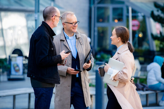 Urban business lifestyle moment: mid-age professionals meeting outdoor, collaborating with laptop and phones, smiling and discussing work over coffee