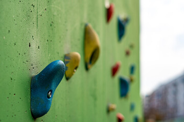 Colorful climbing holds installed on a green recreational wall located within a modern residential housing estate playground area