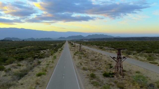 Drone fly along the long straight highway road cutting through a desert valley during the sunset colors, Av. la Mexicana, Chilecito, La Rioja Province, Argentina